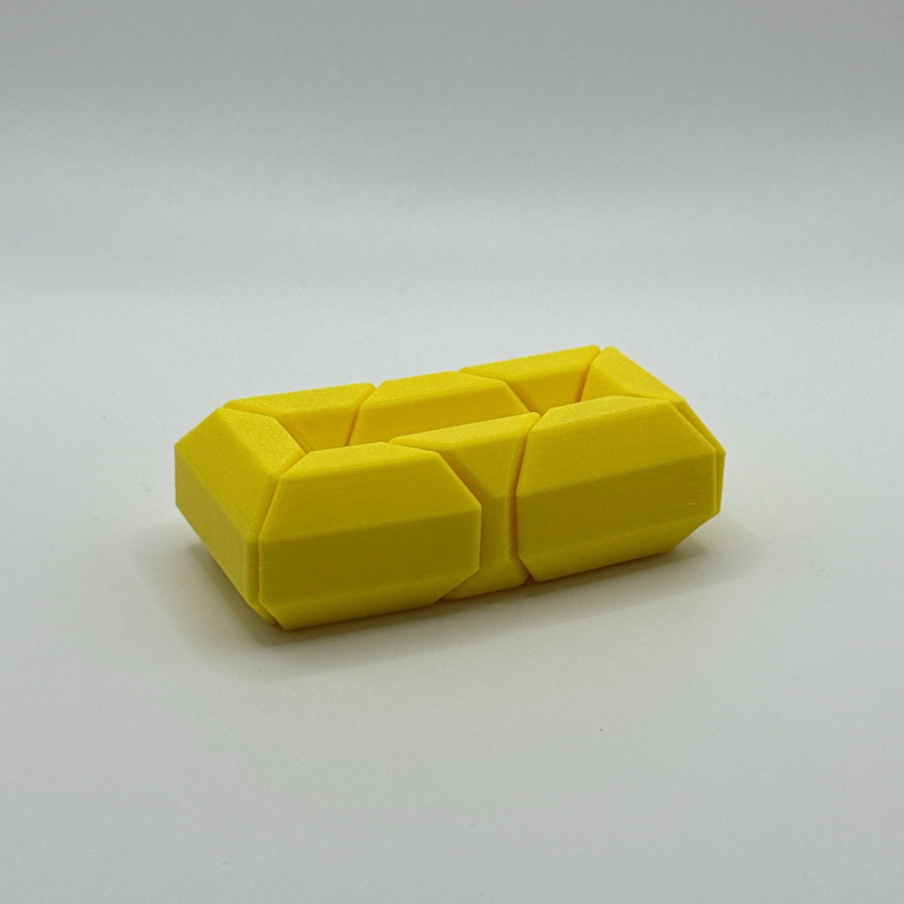 Yellow Infinite Twist hexagon-shaped fidget toy on a white background