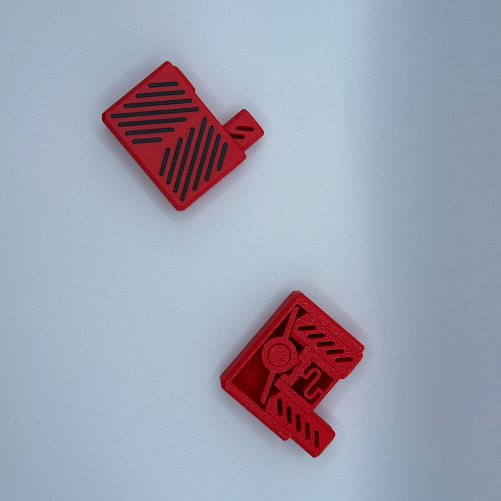 Top down view of two red Clik Clak fidget toys with black patterns slit accents on a light gray background